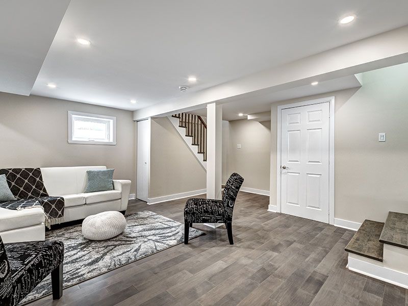 Spacious modern basement living room with sectional sofa, patterned chairs, staircase, and white closet doors