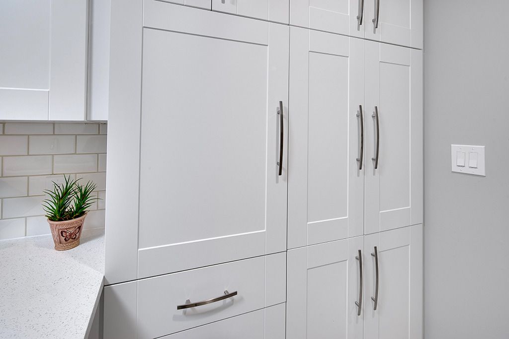 White kitchen cabinets with silver handles and a small potted plant on a countertop, next to a gray wall.