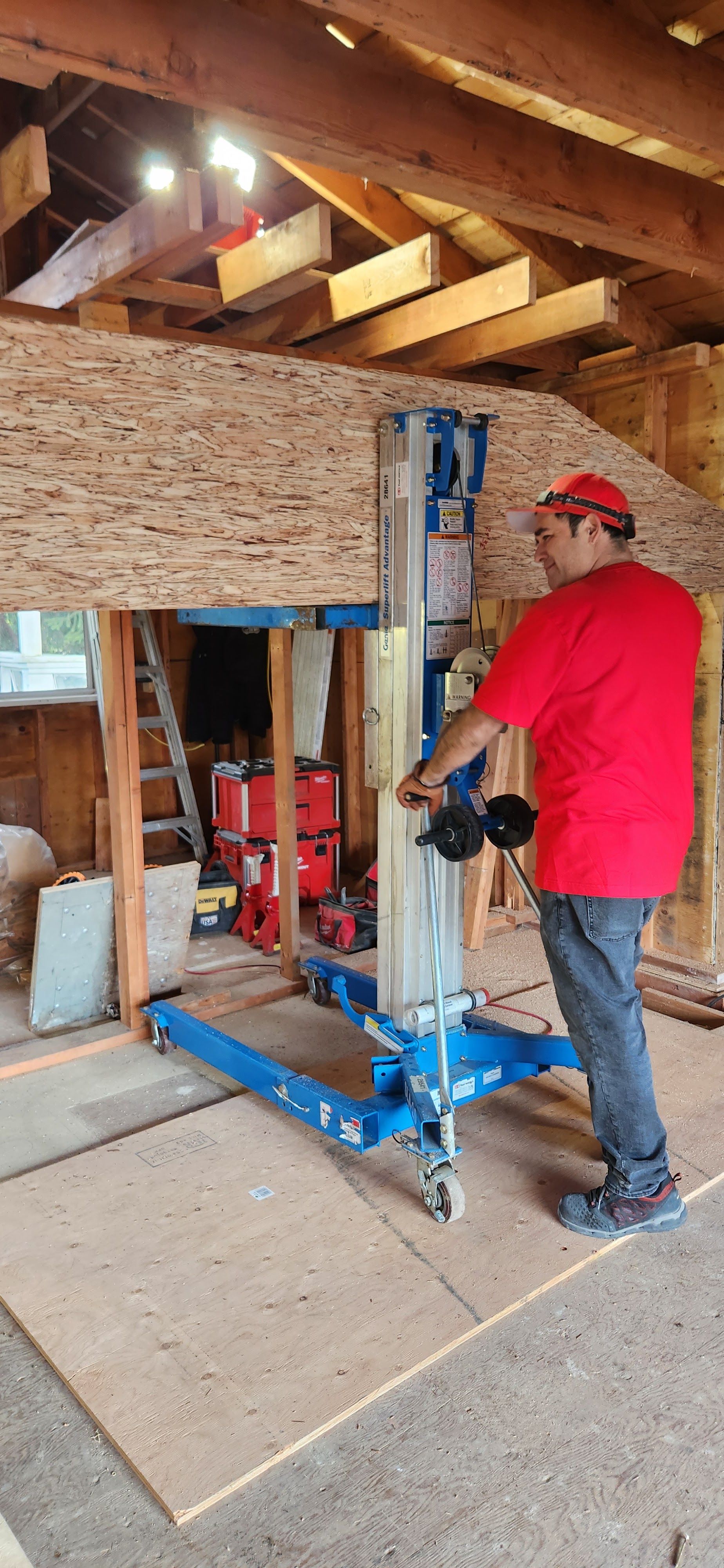 Person in red shirt operating a blue construction lift in a basement with exposed beams