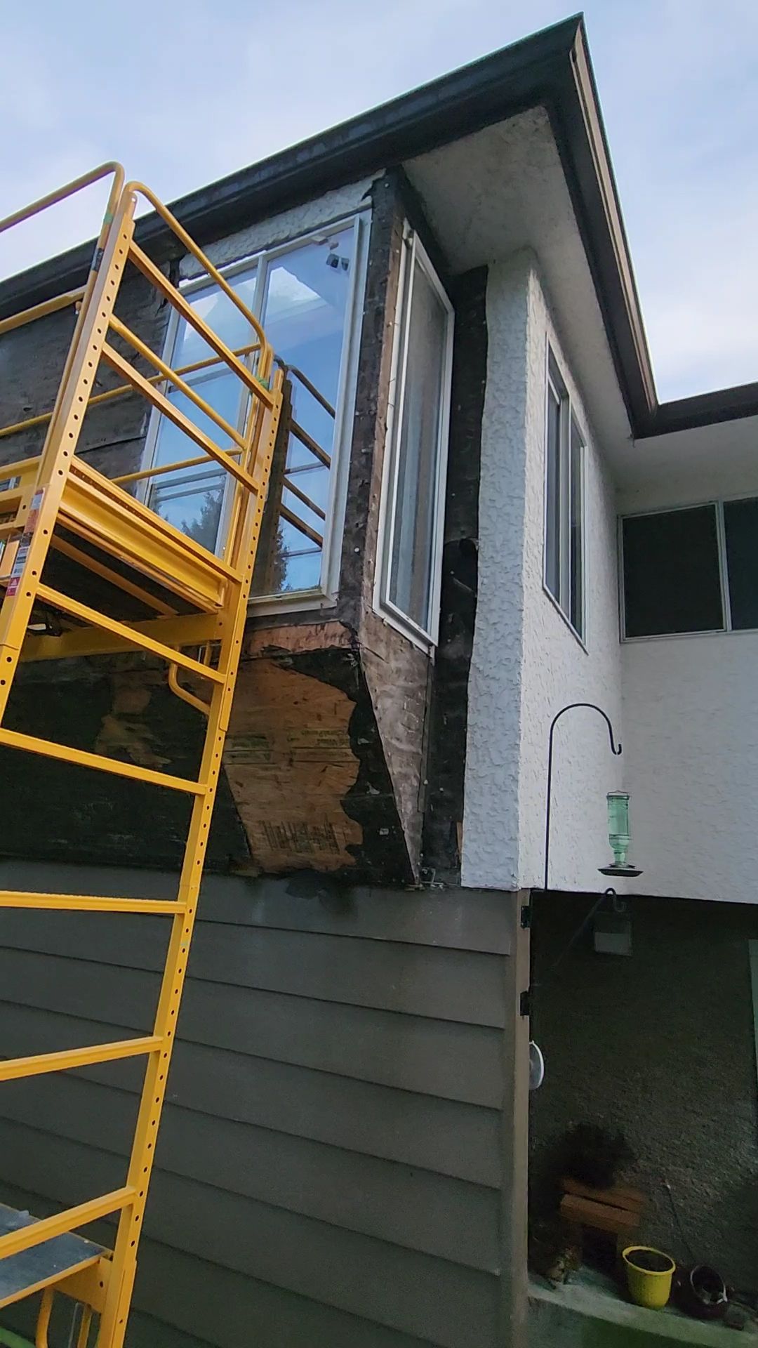 Yellow scaffold beside a house exterior with large windows and dark gray siding