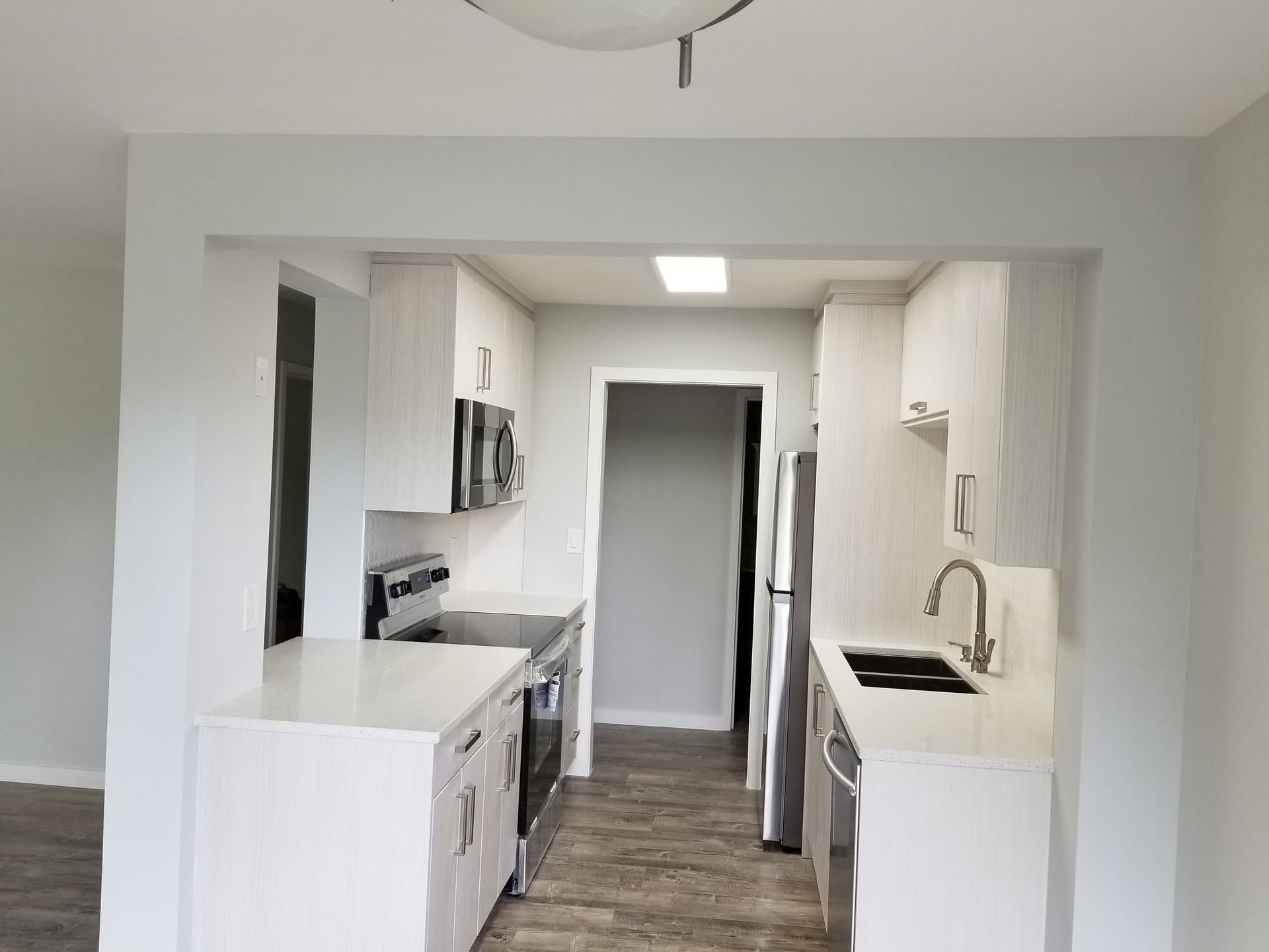 Bright white kitchen with stainless steel appliances and a central view into a hallway.