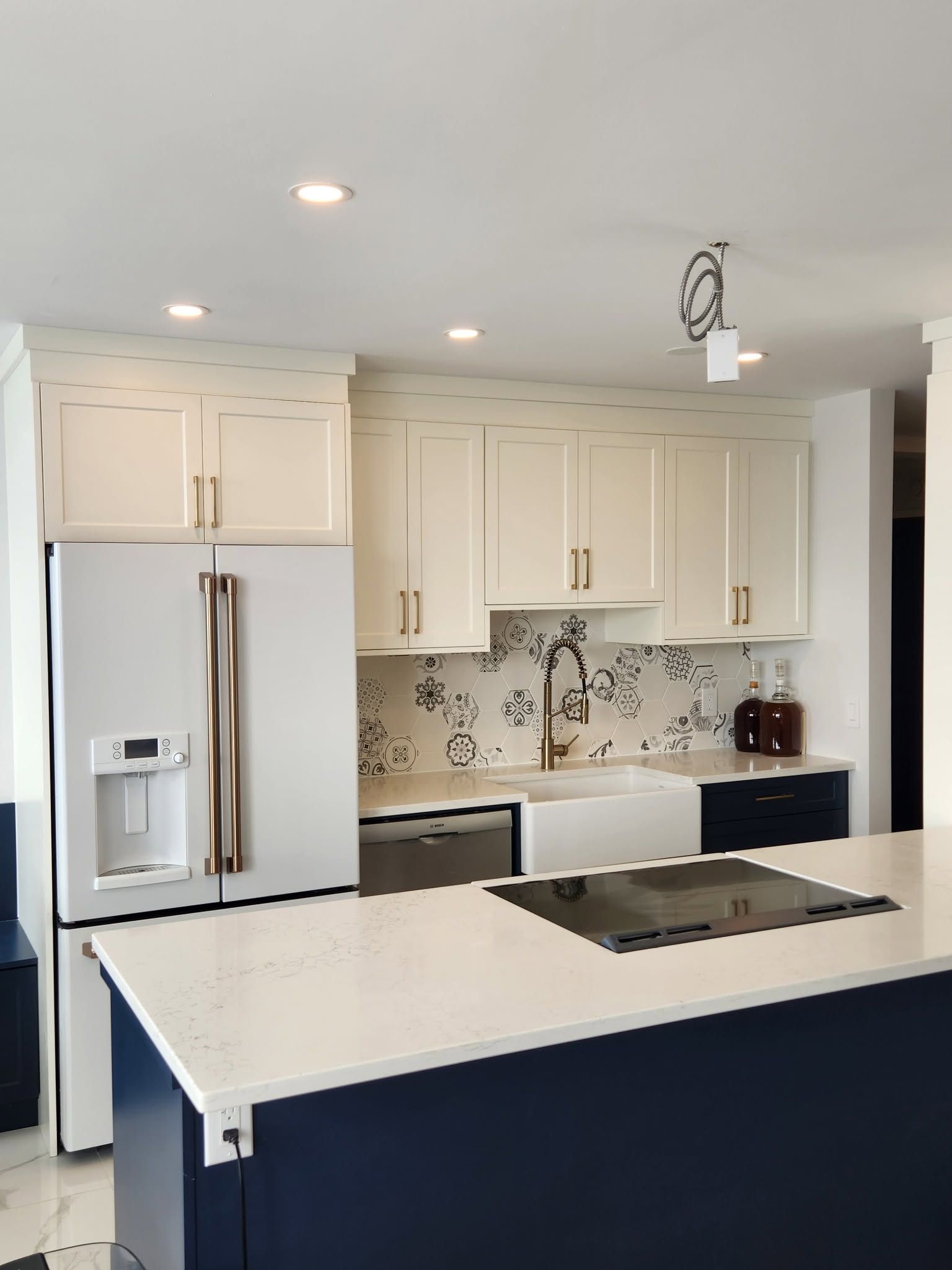 Modern white kitchen with stainless steel appliances, island cooktop, and recessed lighting