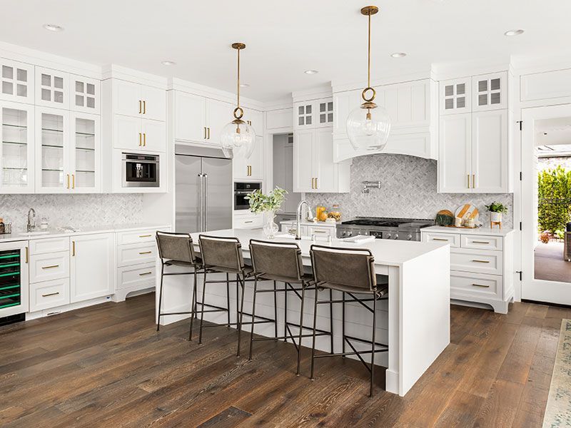 Bright white kitchen with island, bar stools, and dark wood floors