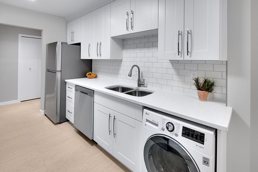 Bright modern kitchen with white cabinets, gray fridge, and front-load washer under the counter.