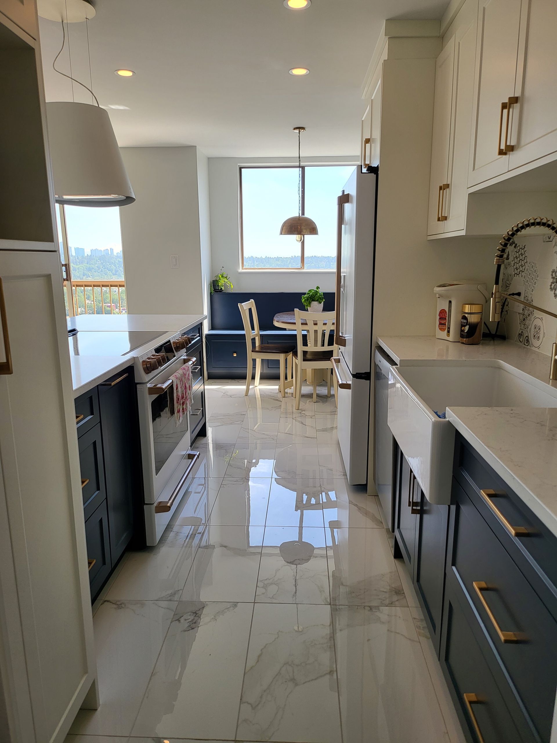 Bright galley kitchen with white cabinets, glossy floor, and a window view of a dining area and ocean beyond