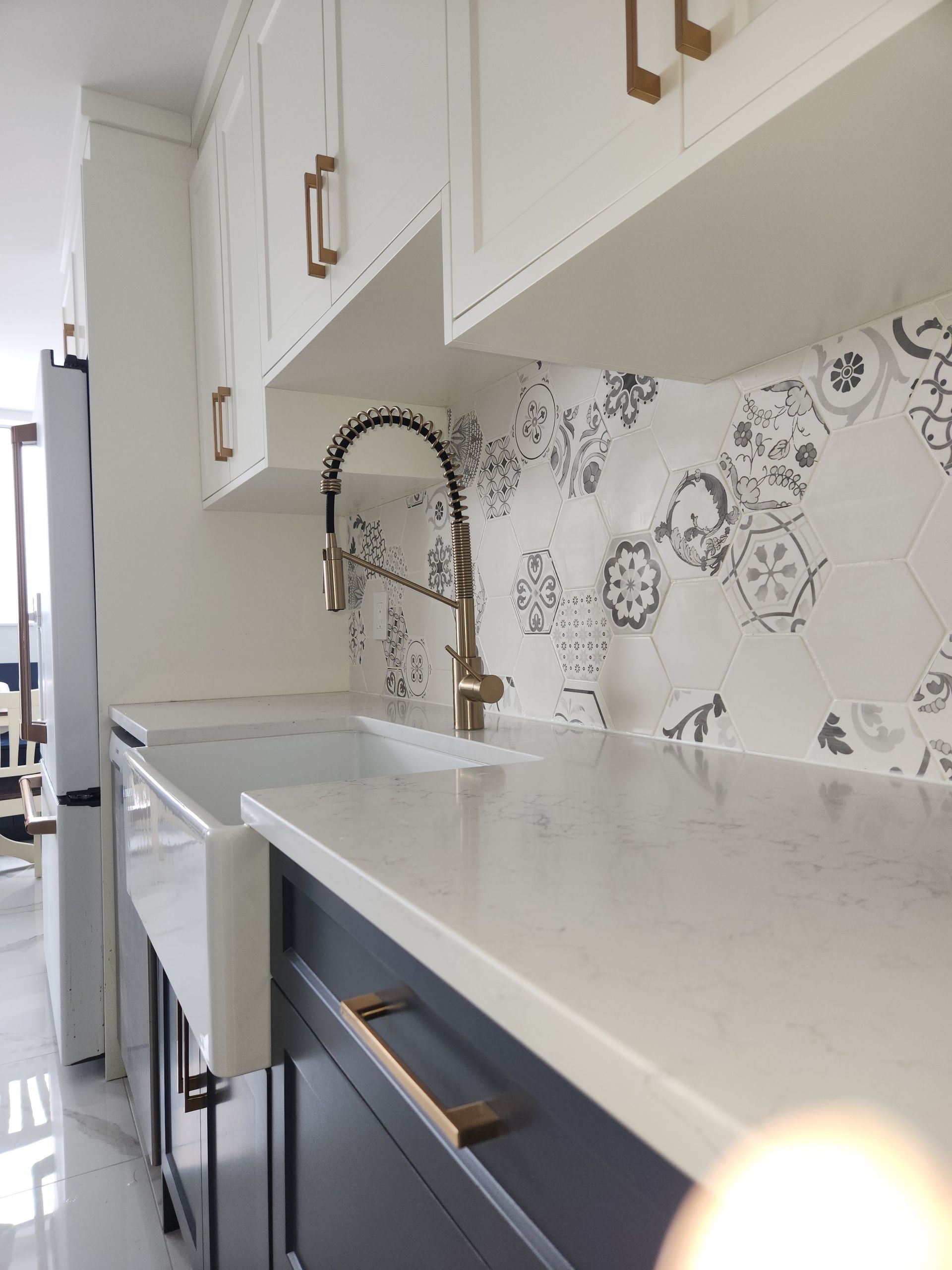 Modern kitchen countertop with brass faucet, white cabinets, and patterned tile backsplash
