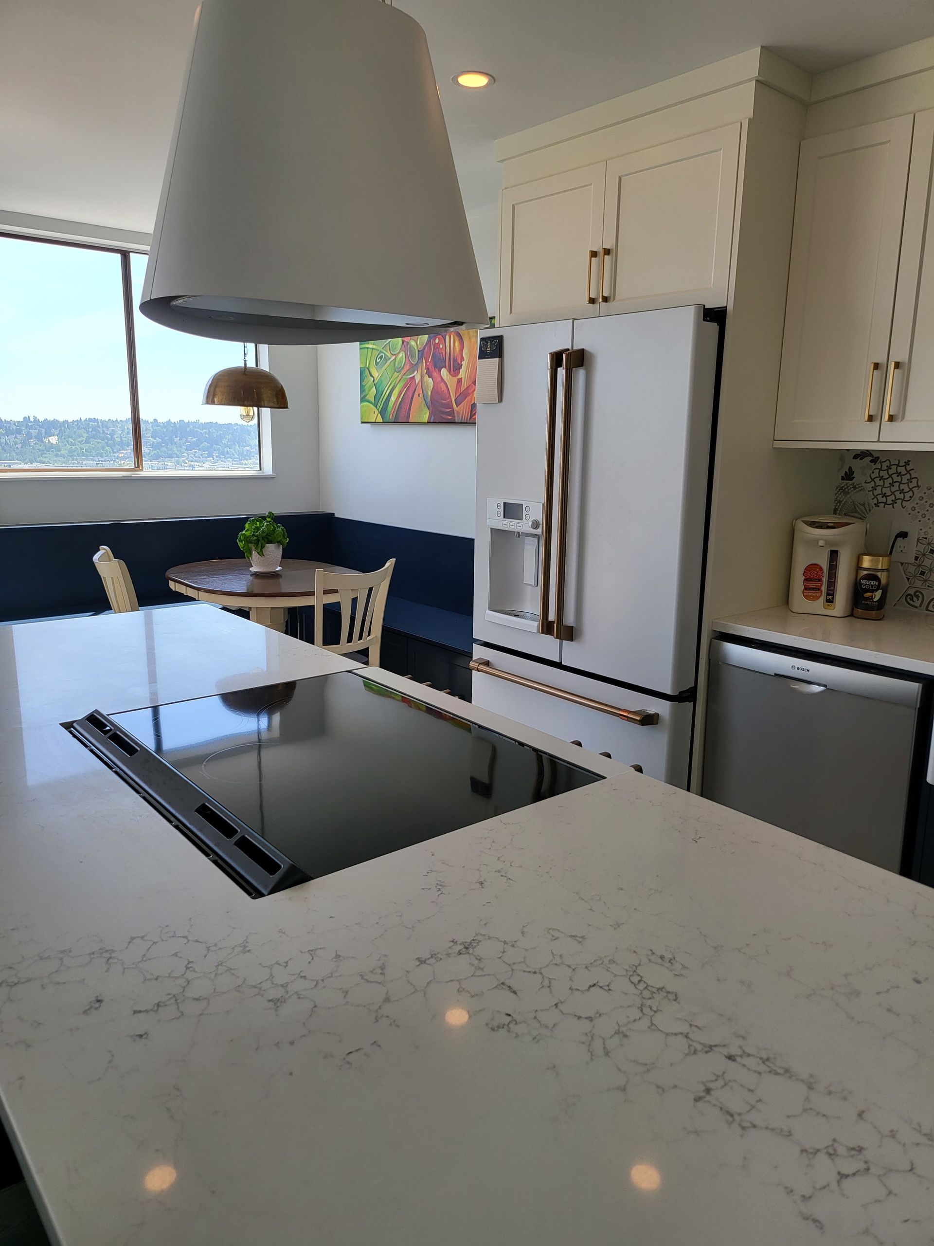 Modern kitchen with white cabinets, stainless fridge, island cooktop, and large window with blue walls.