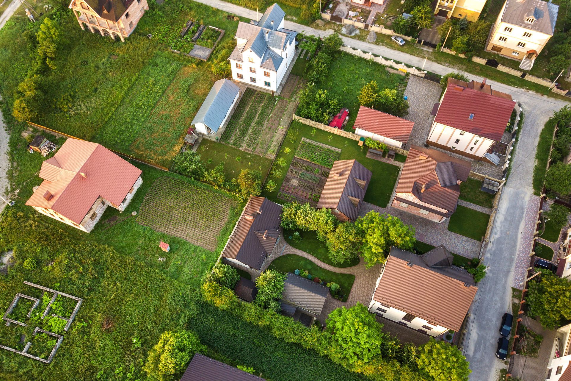 Aerial view of a suburban neighborhood with houses, yards, and roads surrounded by green fields
