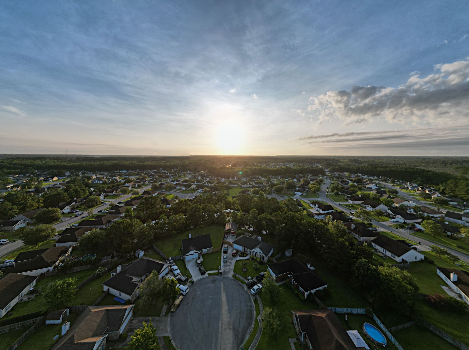 Aerial view of a suburban neighborhood at sunset with scattered clouds and a winding street.