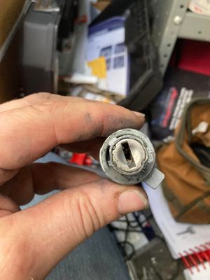 Close-up of a hand holding a worn metal cylinder with a central slot in a cluttered workspace
