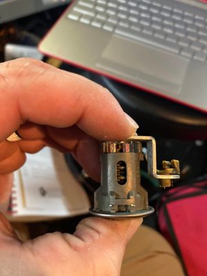 Hand holding a small metal mechanical part with a circuit board in front of a laptop