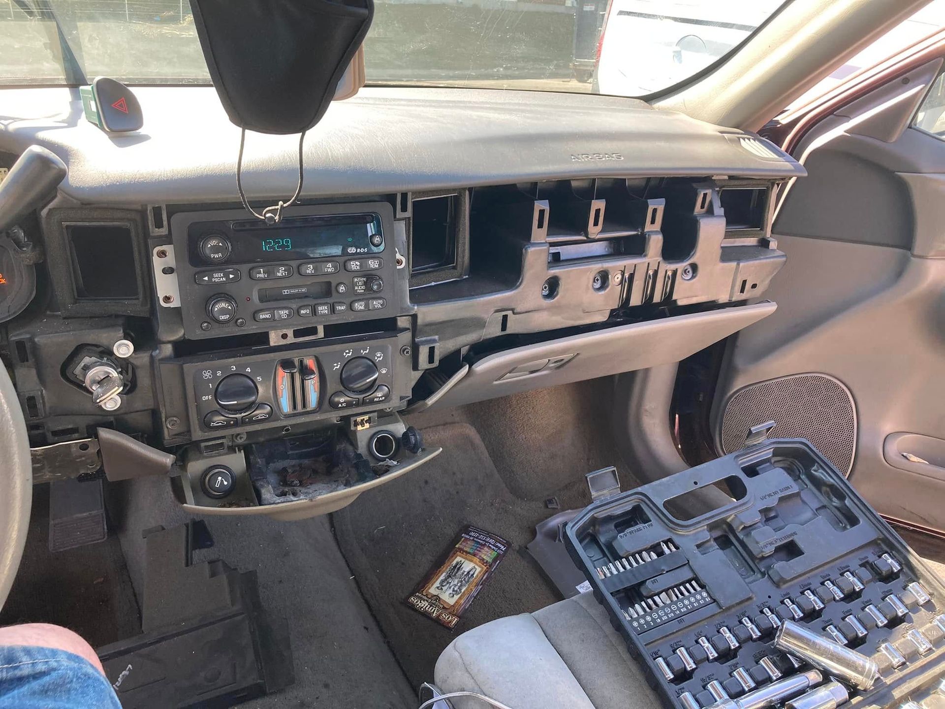 Car interior with dashboard removed, exposing wiring and a black toolbox on the passenger seat.