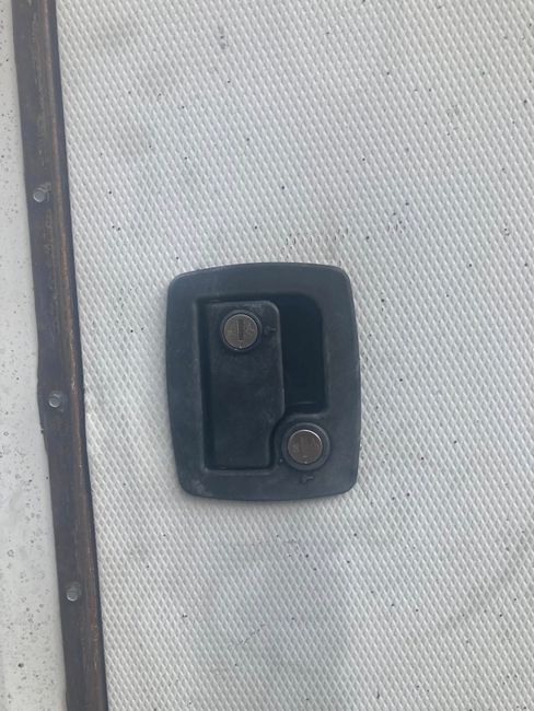 Close-up of a black metal latch mounted on a light gray fabric panel