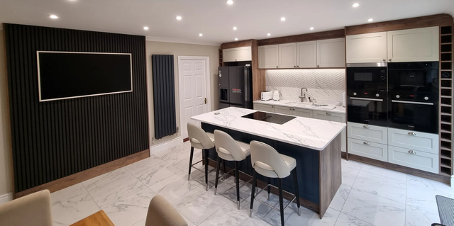 Modern kitchen with island, black pendant chairs, white cabinets, and a dark wood accent wall with TV panel