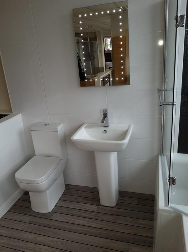 Small modern bathroom with toilet, pedestal sink, mirror, and glass shower enclosure.
