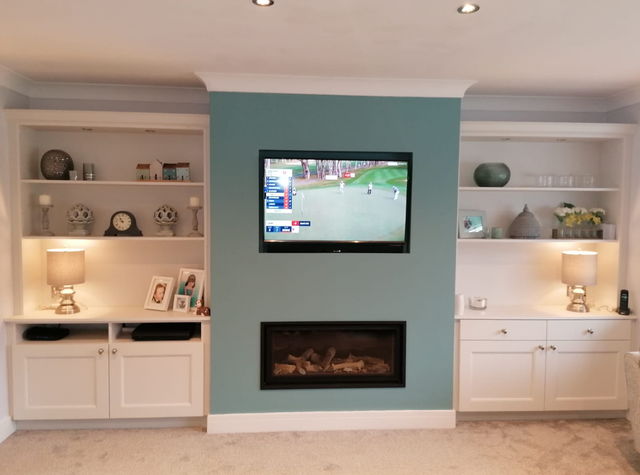Living room with built-in shelves, wall-mounted TV, and fireplace on a teal accent wall