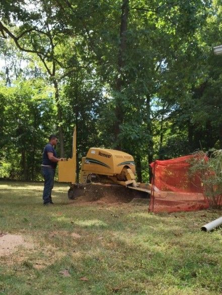 Worker operating a yellow wood chipper beside orange safety fencing in a wooded area