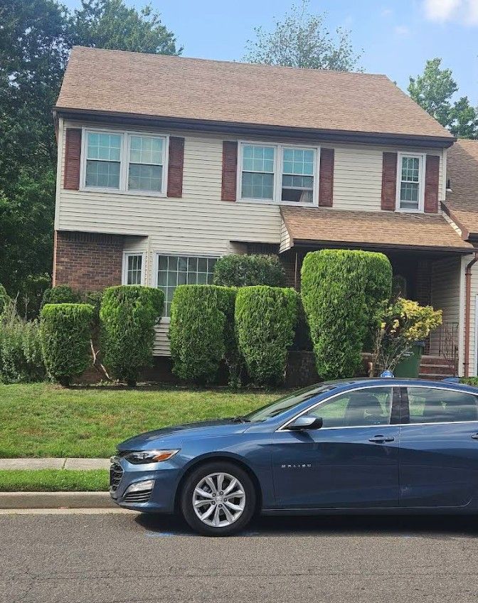 Suburban two-story house with trimmed shrubs; blue sedan parked in front on a sunny day.