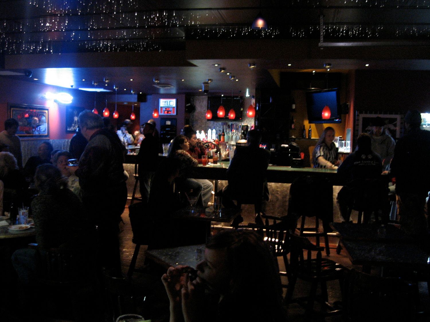 A group of people are gathered at a bar in a dark room