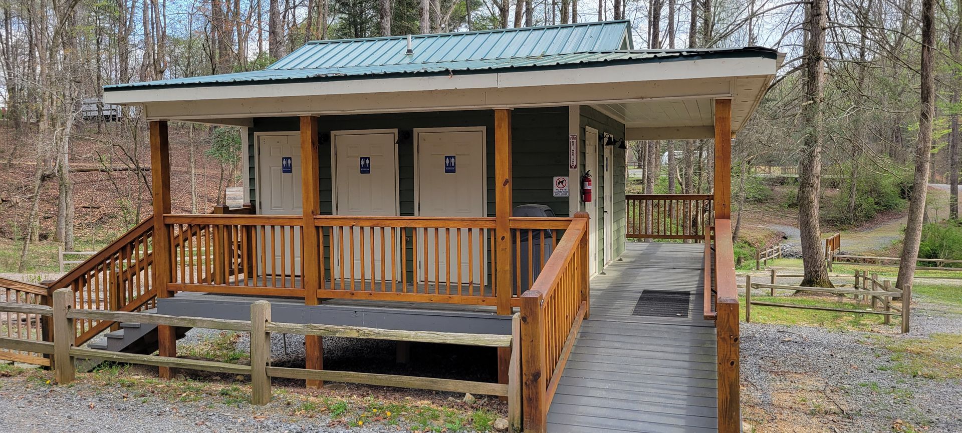Outdoor restroom building with wooden porch, ramp, and green metal roof.