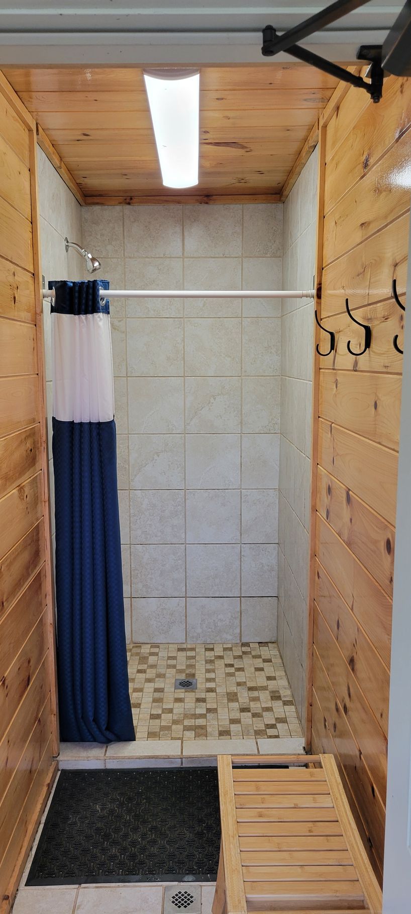 Outdoor shower with wood panel walls, tile, and a dark blue shower curtain.