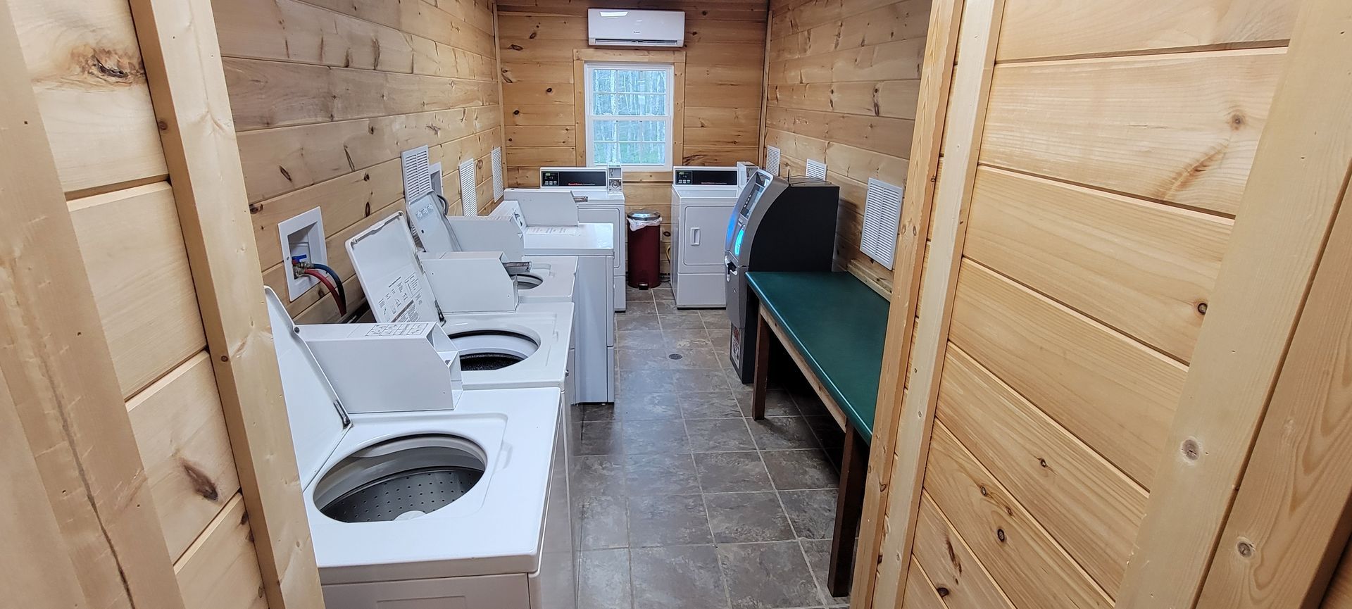 A laundry room with multiple washers and dryers, with a wooden bench on the right side.