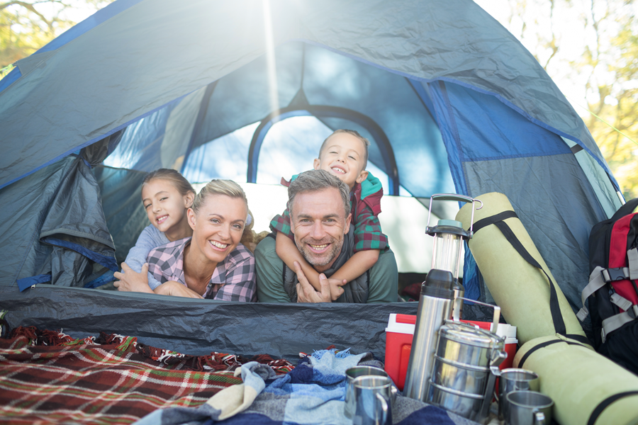 A family is laying in a tent and smiling for the camera