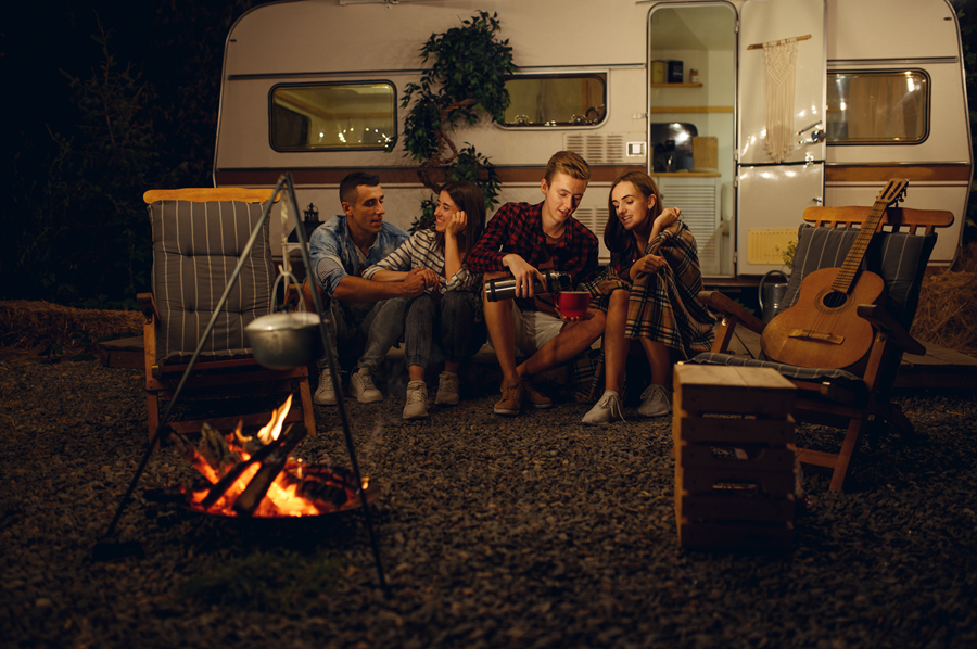 A group of people are sitting around a campfire in front of a trailer