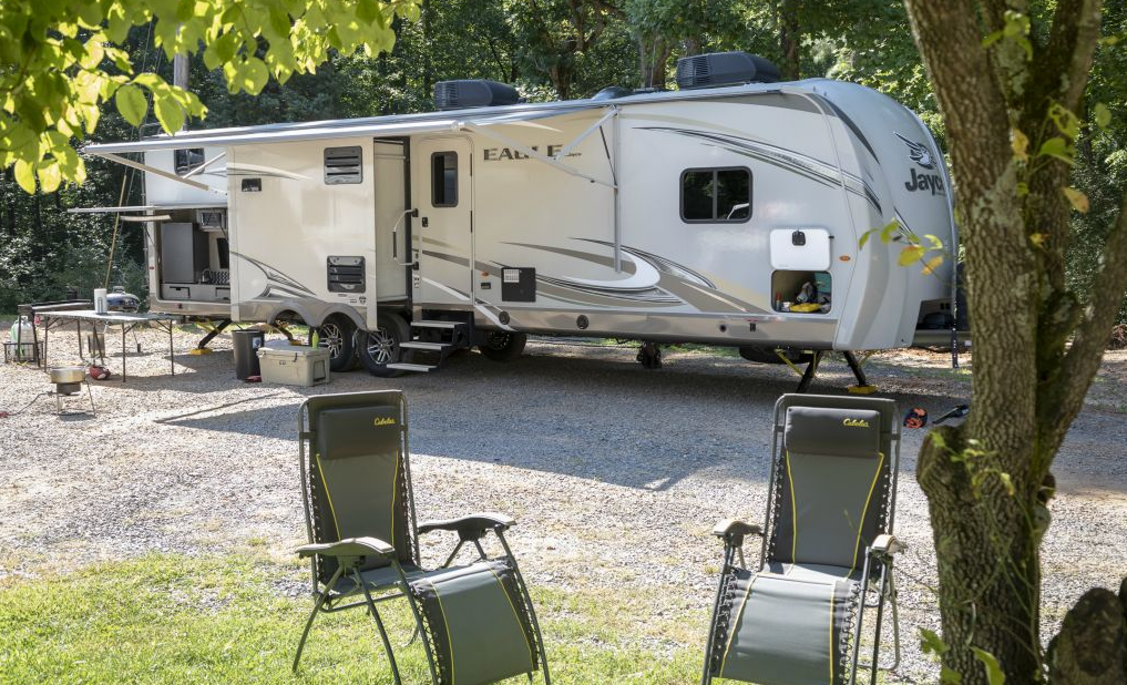 A rv parked in a gravel lot with chairs in front of it