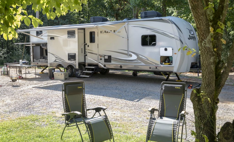 A rv parked in a gravel lot with chairs in front of it