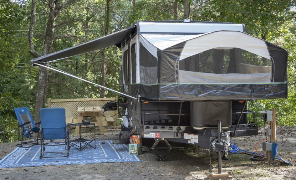A trailer with a tent attached to it is parked in the woods
