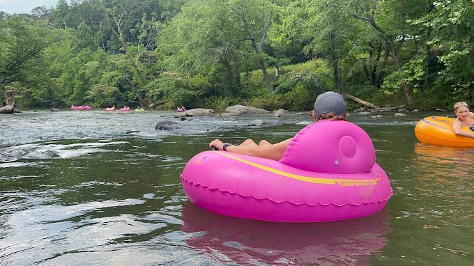 A person is floating on a pink tube in a river.