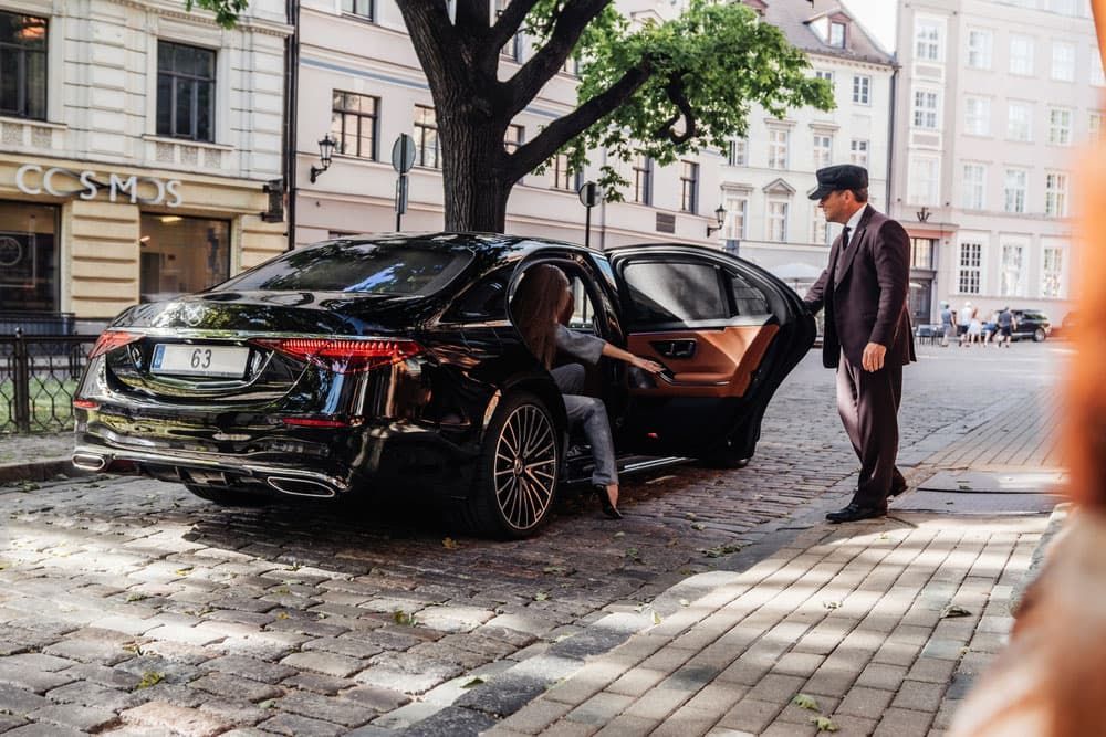 Executive driver opening door to luxury sedan
