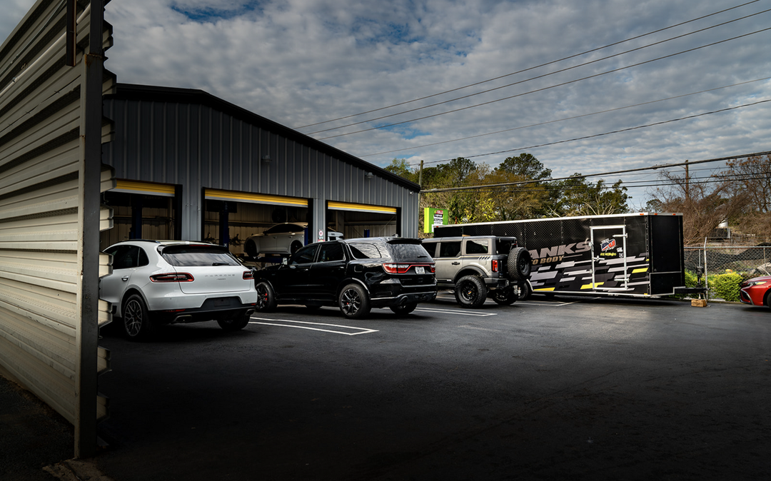 Industrial building parking lot with several parked vehicles and a trailer under a cloudy sky