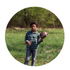 Person standing in a grassy field holding a football, with trees in the background