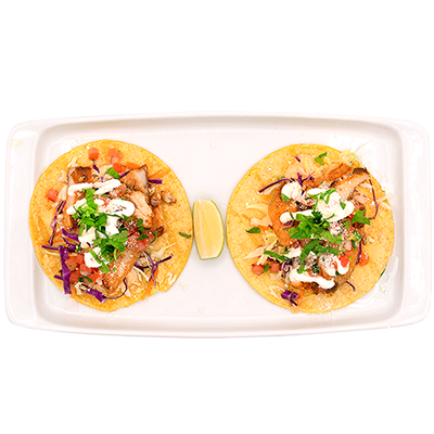 Two tacos on a white tray with a lime wedge, topped with cilantro, onions, and sauce