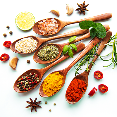 Assorted spices and herbs in wooden spoons with lemon and garlic on a white background