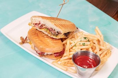 Grilled sandwich and fries on a white plate with ketchup on a turquoise table