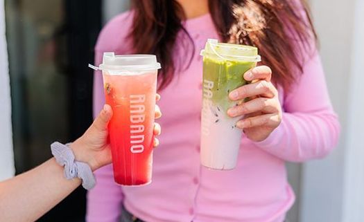 Two hands holding colorful iced drinks, one red and one layered green and white, outdoors