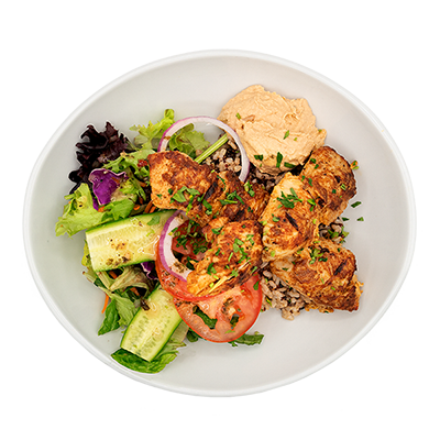 White bowl of grilled chicken over rice and salad with cucumbers, tomatoes, onions, and hummus
