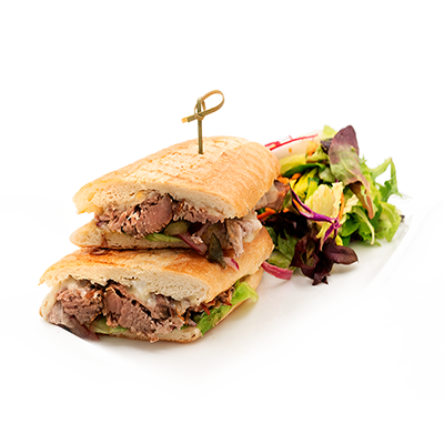 Two beef sandwich halves on a white plate with mixed greens garnish