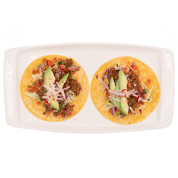 Two tacos on a white plate, topped with meat, greens, and shredded cheese