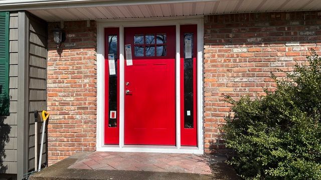 Bright red front door with white trim set in a brick house exterior
