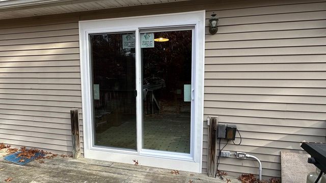 Sliding glass patio door on beige house siding with outdoor utility meters beside it