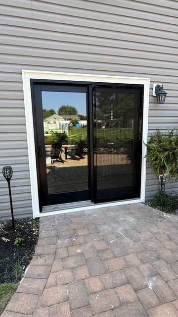 Black sliding glass patio door on a brick patio beside a light siding wall