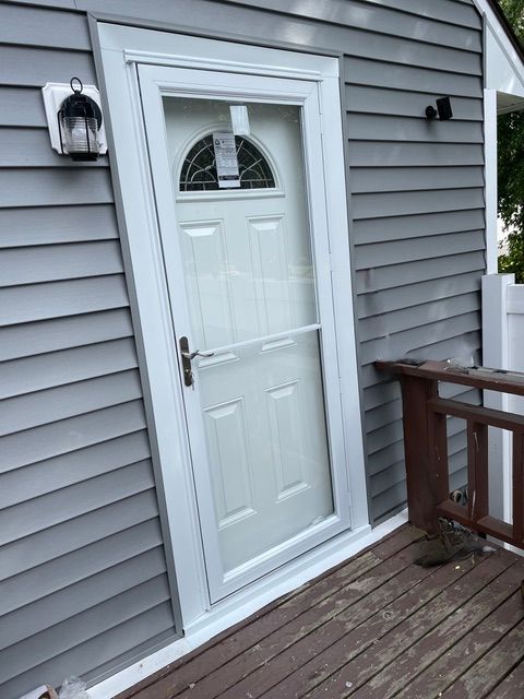 White front door with small window on gray house siding and wooden deck railing
