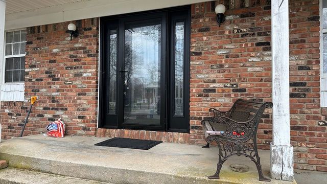 Brick front porch with glass double doors, a bench, and a doormat