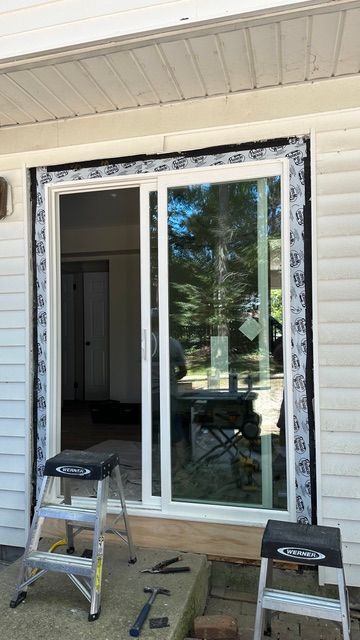Sliding glass door installation with white trim on a house porch, with tools and two step stools nearby