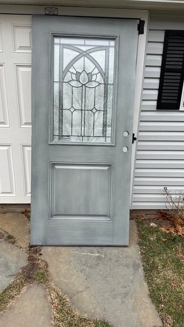 Gray front door with decorative glass panel on a concrete entryway beside white siding