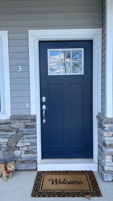 Blue front door with a small window, welcome mat, and house number 3 on a porch.